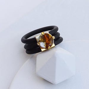 May include: A black silicone ring with three bands and a gold setting with a smoke topaz stone.  SMOKE TOPAZ CRUCKED | YELLOW GOLD