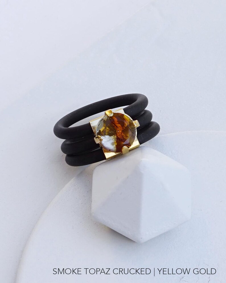 May include: A black silicone ring with three bands and a gold setting with a smoke topaz stone.  SMOKE TOPAZ CRUCKED | YELLOW GOLD