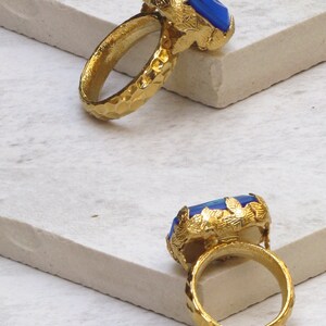 May include: A gold ring with a large blue opaque gemstone set in a leafy design. The ring band is textured with a hammered finish.