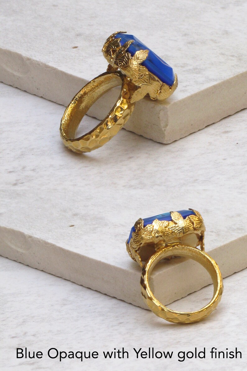 May include: A gold ring with a large blue opaque gemstone set in a leafy design. The ring band is textured with a hammered finish.