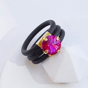 May include: A black silicone ring with three bands and a large fuchsia rhinestone set in yellow gold.