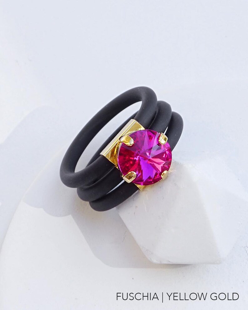 May include: A black silicone ring with three bands and a large fuchsia rhinestone set in yellow gold.
