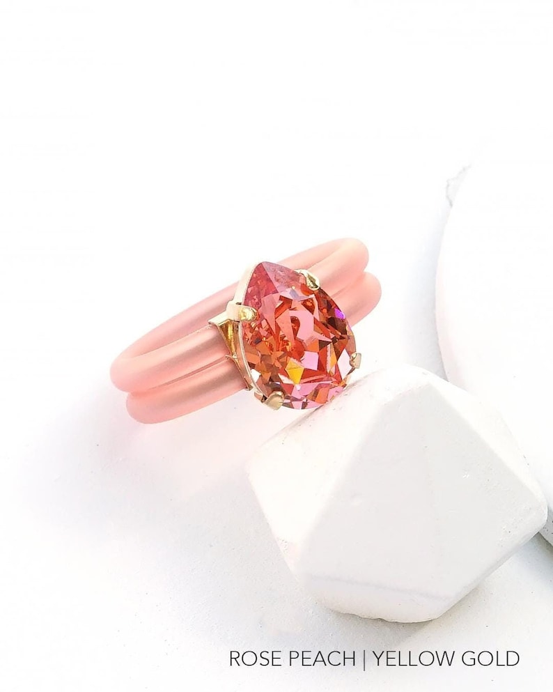 May include: A ring with a pear-shaped, iridescent gemstone set in yellow gold. The ring band is made of a pink silicone material.  ROSE PEACH | YELLOW GOLD