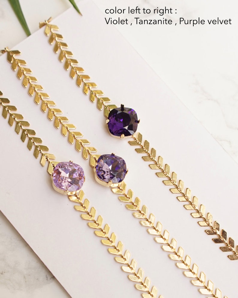 Puede incluir: Tres pulseras doradas con una cadena de patr&oacute;n en espiga y un cristal cuadrado &uacute;nico. Los cristales son de color violeta, tanzanita y purple velvet de izquierda a derecha, seg&uacute;n lo indicado por el texto en la imagen.