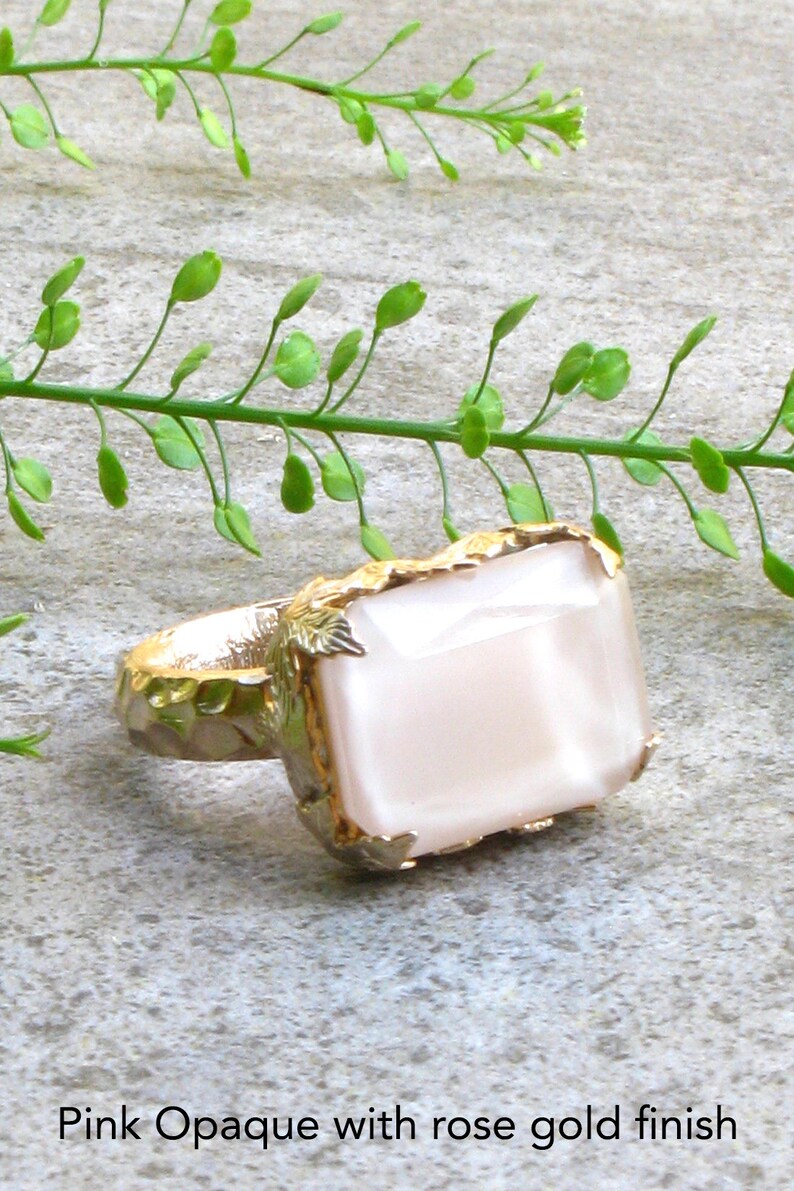 May include: A ring with a large, rectangular, opaque pink stone set in a gold setting with leaf-like details. The ring has a rose gold finish.