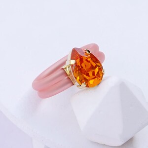 May include: A pink silicone ring with a gold setting and an orange teardrop-shaped gemstone.  ORANGE | YELLOW GOLD