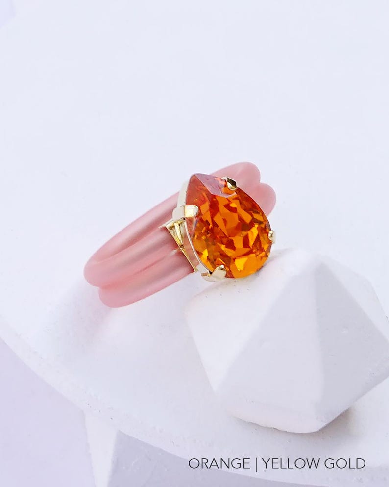May include: A pink silicone ring with a gold setting and an orange teardrop-shaped gemstone.  ORANGE | YELLOW GOLD