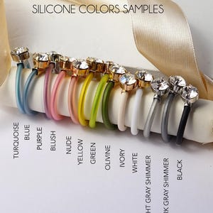 Op de afbeelding: Een collectie siliconen ringen met heldere gefacetteerde stenen, gelabeld HELY DESIGNS SILICONE COLORS SAMPLES. De ringen zijn verkrijgbaar in turquoise, blauw, paars, blush, nude, geel, groen, olivine, ivoor, wit, lichtgrijze glans, donkergrijze glans en zwart.