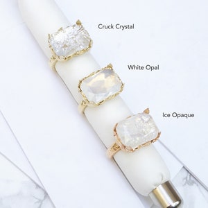 K&ouml;nnte beinhalten: Drei goldene Ringe mit verschiedenen klaren Steinen. Die Steine sind mit "Cruck Crystal", "White Opal" und "Ice Opaque" beschriftet.