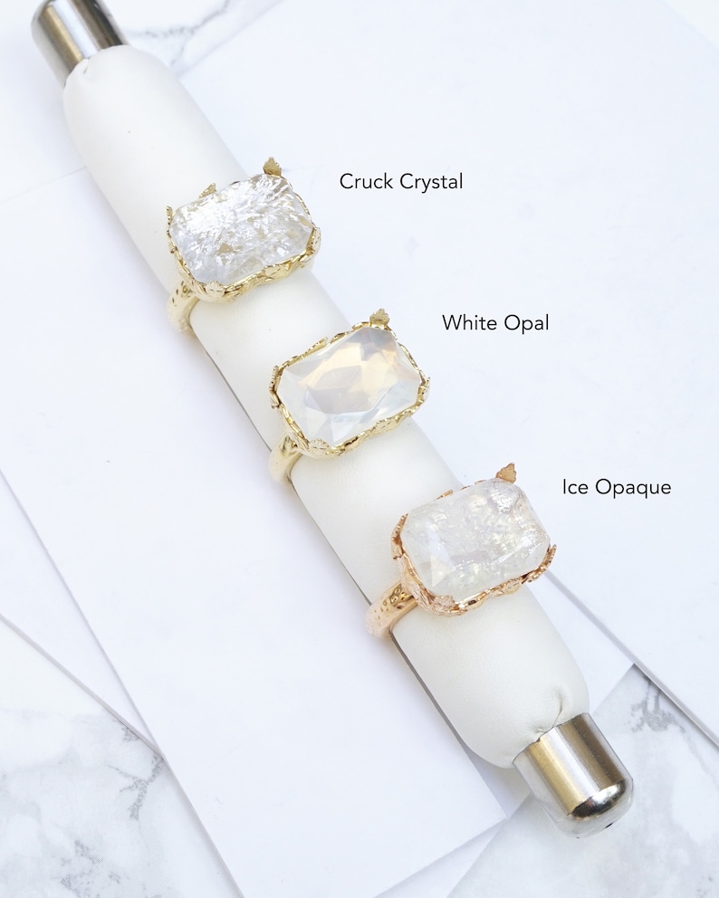 K&ouml;nnte beinhalten: Drei goldene Ringe mit verschiedenen klaren Steinen. Die Steine sind mit "Cruck Crystal", "White Opal" und "Ice Opaque" beschriftet.