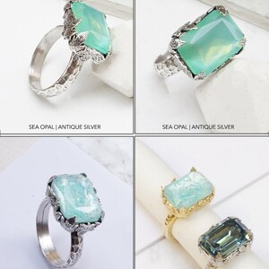 May include: Four silver rings with different gemstones. The top left ring features a sea opal gemstone with a leafy design. The top right ring features a sea opal gemstone with a leafy design. The bottom left ring features a lagoon gemstone with a leafy design. The bottom right ring features an Indian sapphire gemstone with a leafy design.