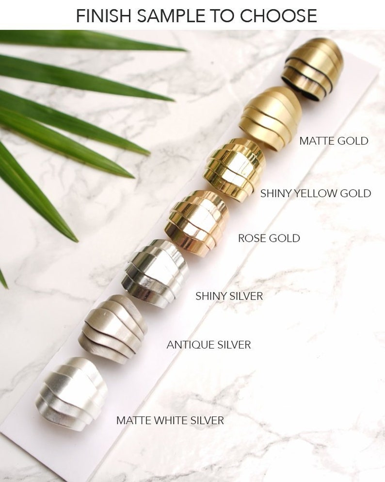 May include: A collection of six metal rings arranged in a row on a white card, labeled FINISH SAMPLE TO CHOOSE. The finishes include matte gold, shiny yellow gold, rose gold, shiny silver, antique silver, and matte white silver.