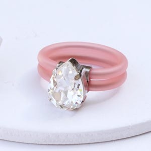 May include: A pink silicone ring with a clear pear-shaped crystal. The ring is double-banded and has a silver setting for the crystal. CLEAR | SILVER