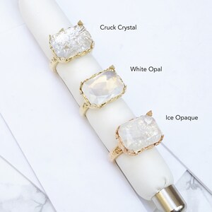May include: Three gold rings with different clear stones. The stones are labeled "Cruck Crystal", "White Opal", and "Ice Opaque".