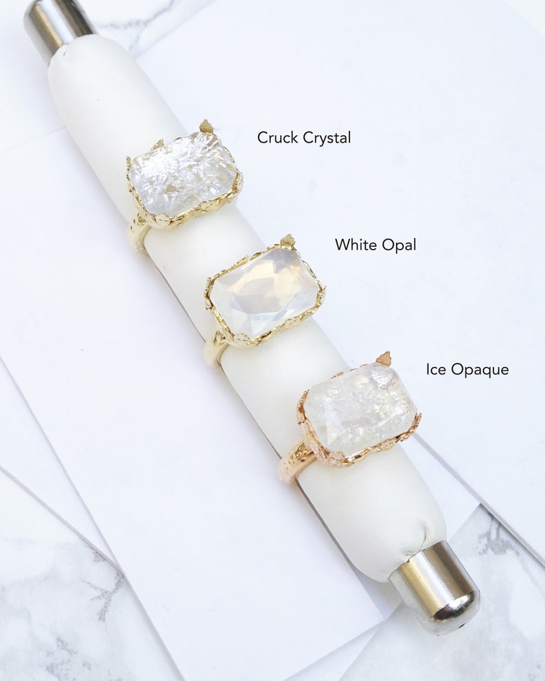 May include: Three gold rings with different clear stones. The stones are labeled "Cruck Crystal", "White Opal", and "Ice Opaque".