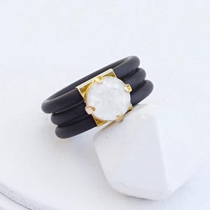 May include: A black silicone ring with three bands and a white marble stone set in yellow gold.