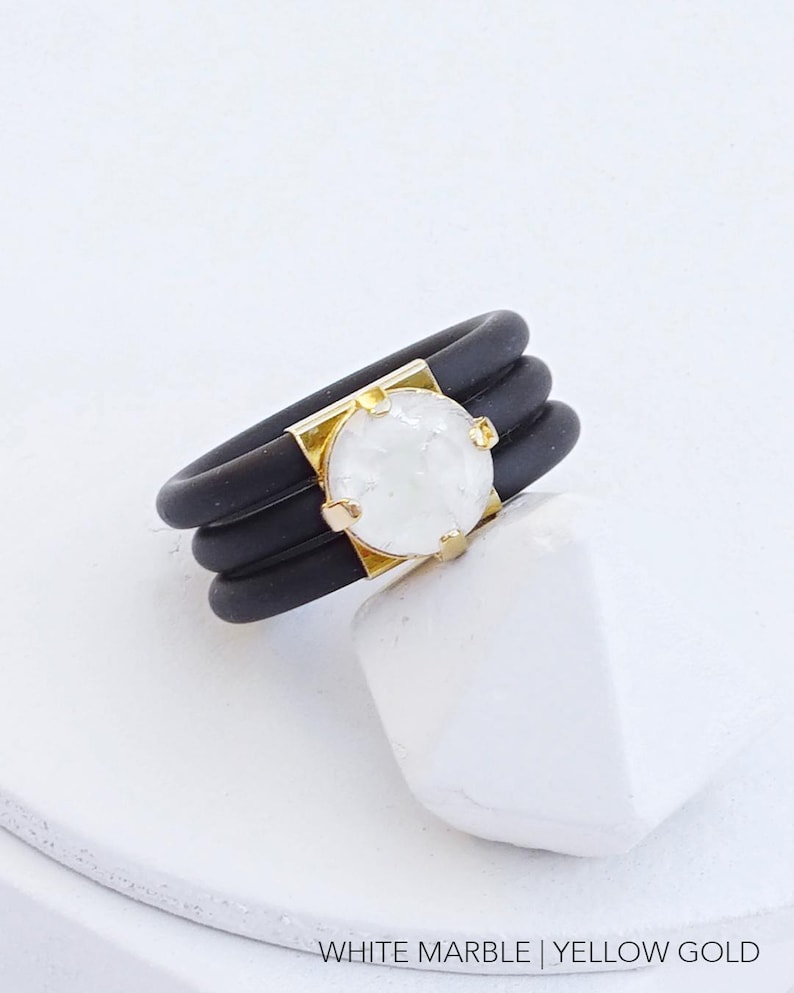May include: A black silicone ring with three bands and a white marble stone set in yellow gold.