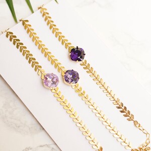 Puede incluir: Tres pulseras doradas con una cadena de patr&oacute;n en espiga y un cristal cuadrado individual. Los cristales est&aacute;n dispuestos de izquierda a derecha en colores violeta, tanzanita y terciopelo p&uacute;rpura. Cada pulsera incluye un cierre de mosquet&oacute;n.