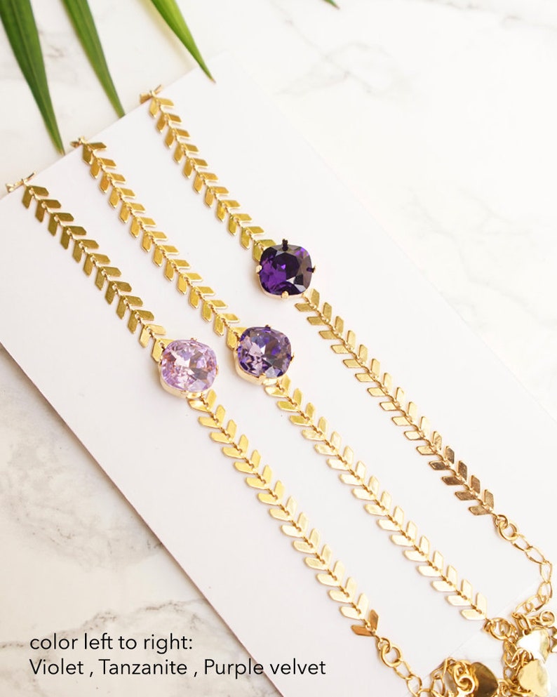Puede incluir: Tres pulseras doradas con una cadena de patr&oacute;n en espiga y un cristal cuadrado individual. Los cristales est&aacute;n dispuestos de izquierda a derecha en colores violeta, tanzanita y terciopelo p&uacute;rpura. Cada pulsera incluye un cierre de mosquet&oacute;n.