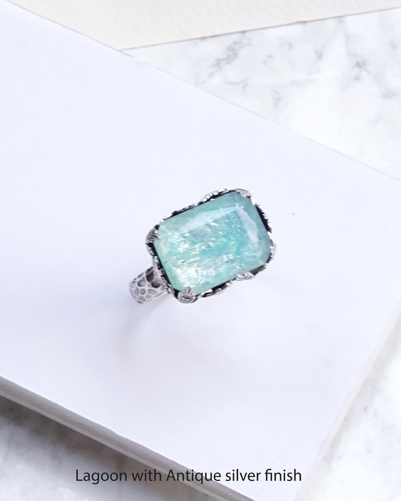 K&ouml;nnte beinhalten: Ein quadratischer Ring mit einem hellblauen Edelstein, der in einer antiken Silberfassung gefasst ist. Der Ring hat ein strukturiertes Band.