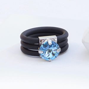 May include: A black silicone ring with three bands and a silver setting with a light blue aquamarine gemstone.