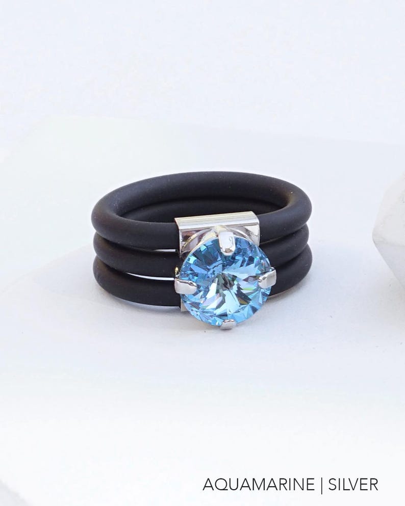 May include: A black silicone ring with three bands and a silver setting with a light blue aquamarine gemstone.