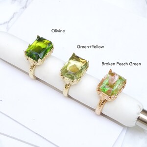 May include: Three gold rings with different colored green glass stones. The rings are labeled "Olivine", "Green+Yellow", and "Broken Peach Green".