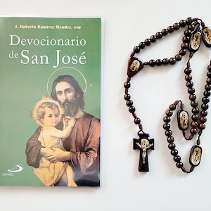 May include: A brown wooden rosary with a crucifix and small images of saints. A green book titled "Devocionario de San José" by J. Roberto Ramirez Mendez, ssp is also pictured.