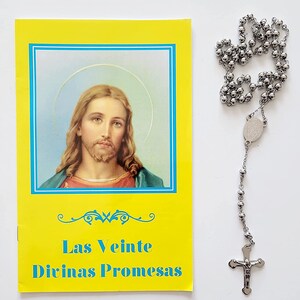 May include: A yellow booklet with a picture of Jesus on the front. The booklet is titled "Las Veinte Divinas Promesas". A silver rosary with a silver cross is next to the booklet.