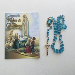May include: A blue rosary with a silver crucifix and a small image of the Virgin Mary. The rosary is next to a booklet titled "Novena a la Virgen de Fatima".