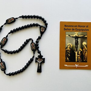 May include: Black wooden rosary beads with a crucifix and images of saints. The rosary is accompanied by a pamphlet titled "Novena en Honor al Señor de Esquipulas".