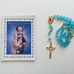 May include: A blue rosary with a gold cross and a small image of a baby. The rosary is accompanied by a booklet titled "Rosario De Los No Nacidos".