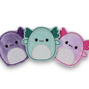 May include: Three plush axolotl toys, each with a different color: purple, teal, and pink. The axolotls have embroidered eyes and mouths, and each has a white belly.