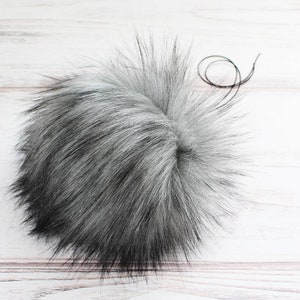 May include: A fluffy gray and black faux fur pom pom with a black thread attached.