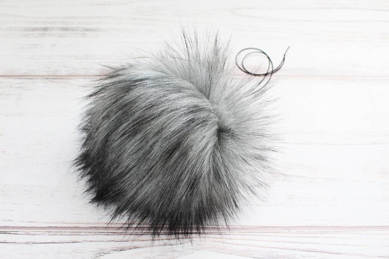 May include: A fluffy gray and black faux fur pom pom with a black thread attached.