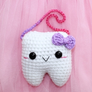 May include: White crocheted tooth with a purple bow, black eyes, and a pink and purple yarn strap.