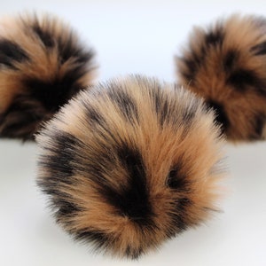 May include: Three brown and black faux fur pom poms. The pom poms are fluffy and soft.