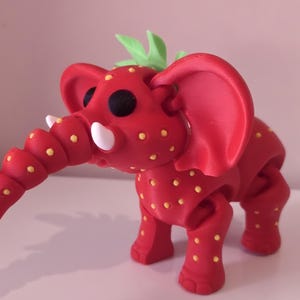 May include: A quirky red elephant ornament, adorned with yellow spots, black eyes, and white tusks. The elephant has a curled trunk, large ears, and green leaves. A distinctive decorative piece.