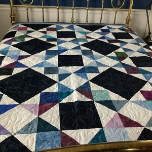 May include: A quilt with a geometric pattern of triangles and diamonds in shades of blue, purple, and white. The quilt is made with a variety of fabrics and has a quilted design.