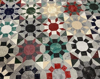 Puede incluir: Una colcha con un patrón geométrico que presenta una variedad de colores, incluyendo rojo, verde, azul y gris. La colcha está hecha de cuadrados y triángulos, y el patrón se repite en toda la colcha.