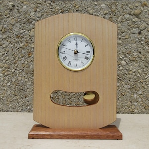 May include: A wooden clock with a pendulum and a gold-coloured face. The clock is made of light wood with a darker wood base. The clock face has Roman numerals and the words "QUARTZ" printed on it.
