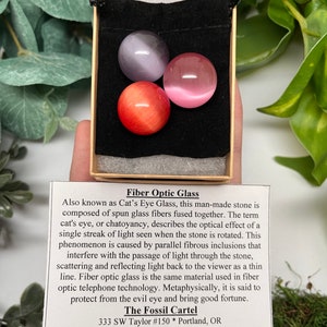 K&ouml;nnte beinhalten: Drei Glaskugeln mit Lichtleitfasern in einem Samtbeutel. Die Kugeln sind lila, rosa und orange. Der Beutel befindet sich in einer kleinen Schachtel. Der Text auf der Schachtel lautet "Fiber Optic Glass", "Also known as Cat's Eye Glass", "The Fossil Cartel", "333 SW Taylor #150 * Portland, OR", "(503) 228-6998 * www.fossilcartel.com".