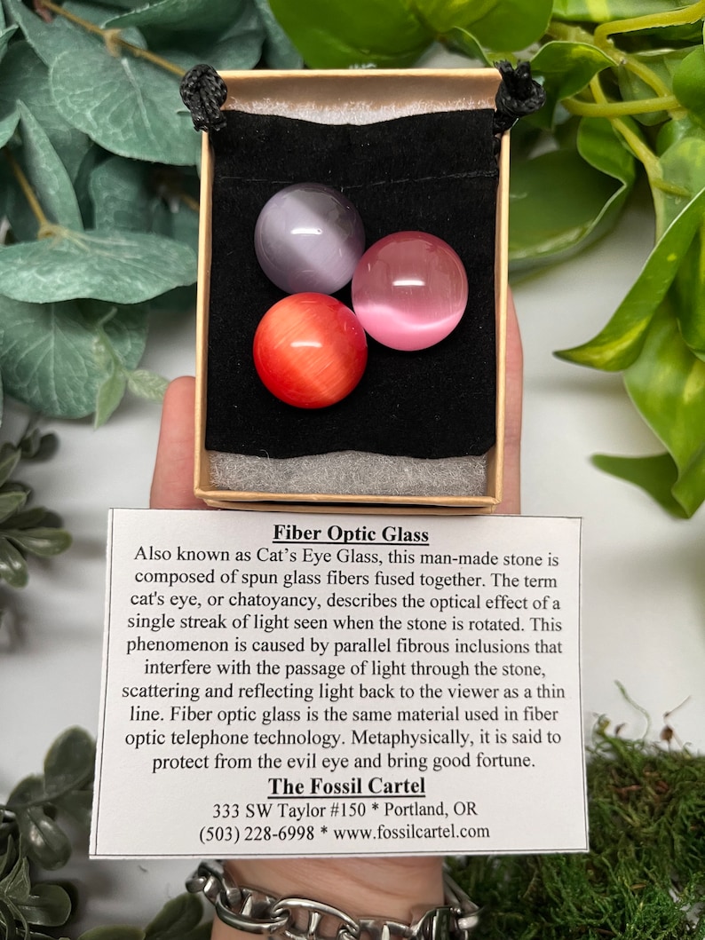K&ouml;nnte beinhalten: Drei Glaskugeln mit Lichtleitfasern in einem Samtbeutel. Die Kugeln sind lila, rosa und orange. Der Beutel befindet sich in einer kleinen Schachtel. Der Text auf der Schachtel lautet "Fiber Optic Glass", "Also known as Cat's Eye Glass", "The Fossil Cartel", "333 SW Taylor #150 * Portland, OR", "(503) 228-6998 * www.fossilcartel.com".