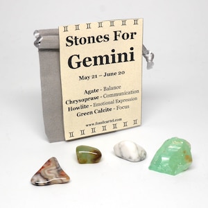 Könnte beinhalten: Ein kleiner grauer Beutel mit einem braunen Etikett, auf dem steht "Stones For Gemini May 21 - June 20 Agate - Balance Chrysoprase - Communication Howlite - Emotional Expression Green Calcite - Focus www.fossilcartel.com". Der Beutel enthält vier kleine Steine: Achat, Chrysopras, Howlith und grüner Calcit.