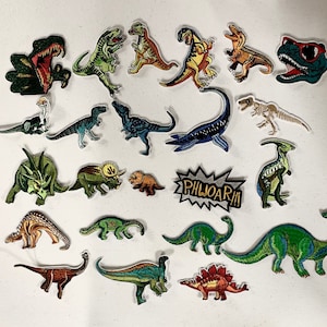 May include: A collection of 18 colorful dinosaur iron-on patches. The patches feature various dinosaurs in different poses, including a T-Rex, a Stegosaurus, and a Triceratops. The patches are perfect for adding a fun and unique touch to clothing, bags, and other accessories.