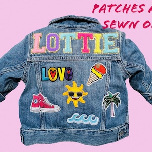 May include: A blue denim jacket with colorful patches sewn on. The patches include the name "Lottie", a heart with the word "Love", a sun with sunglasses, an ice cream cone, a palm tree, and a wave.