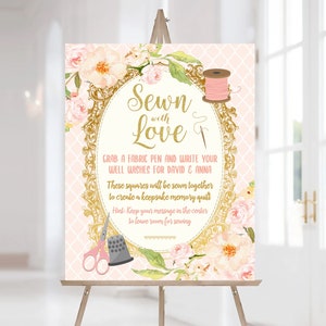 Puede incluir: Un cartel rosa y dorado con detalles florales y el texto "Sewn with Love &"  Se invita a los invitados a tomar un bolígrafo de tela y escribir sus buenos deseos para David y Anna. Estos cuadrados se coserán juntos para crear una colcha de recuerdo.  Sugerencia: Mantenga su mensaje en el centro para dejar espacio para coser.