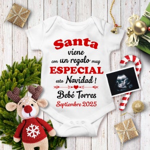 May include: White baby onesie with red text that reads "Santa viene con un regalo muy ESPECIAL esta Navidad! Bebe Torres Septiembre 2025". A red heart is between two arrows. A black and white ultrasound image is in the upper right corner.