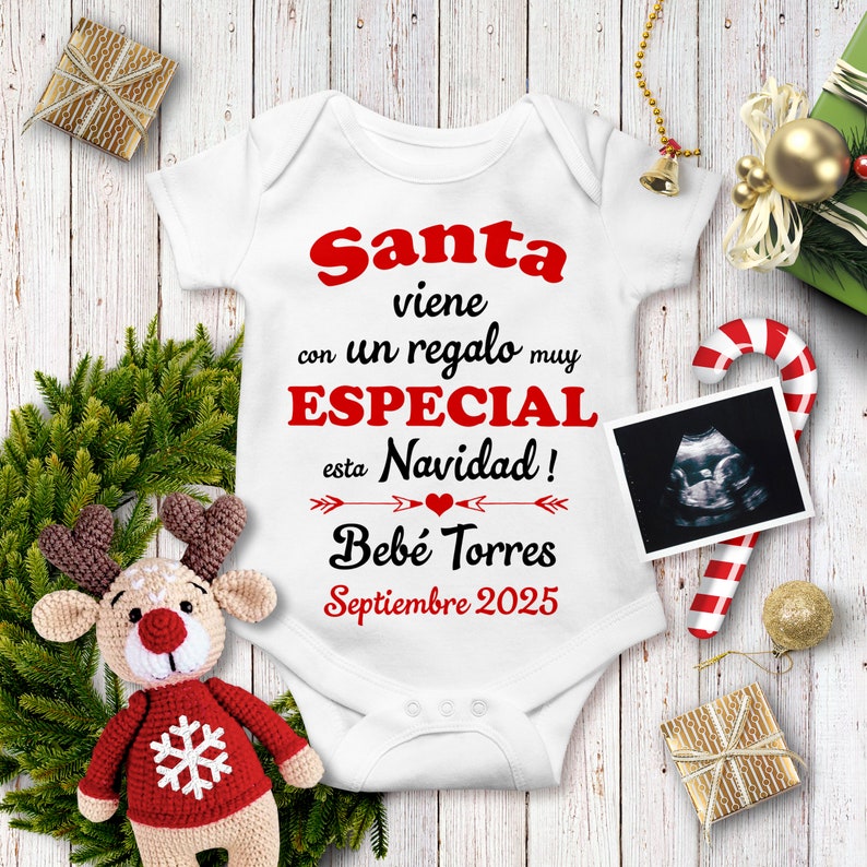 May include: White baby onesie with red text that reads "Santa viene con un regalo muy ESPECIAL esta Navidad! Bebe Torres Septiembre 2025". A red heart is between two arrows. A black and white ultrasound image is in the upper right corner.