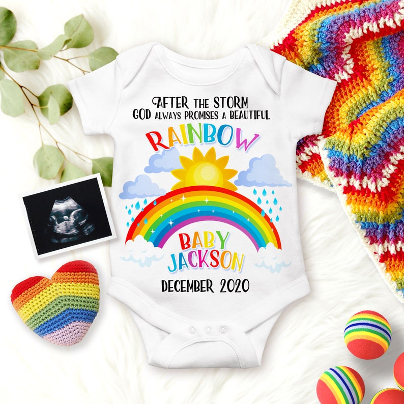 May include: White baby onesie with a rainbow, clouds, sun, and raindrops. The text reads "After the storm God always promises a beautiful rainbow Baby Jackson December 2020".